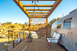 A wooden deck with two white lounge chairs, a potted plant, and a pergola with hanging lights. - Valley Nomads (Valle de Guadalupe)