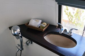 Un baño con tocador de madera oscura, un lavabo, cabezal de ducha y ventana con vistas a la vegetación.