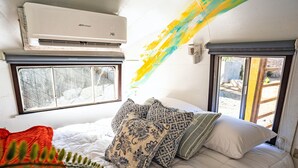 Une chambre à coucher avec un lit, des oreillers, un appareil de climatisation, une fenêtre et une vue sur l’extérieur.