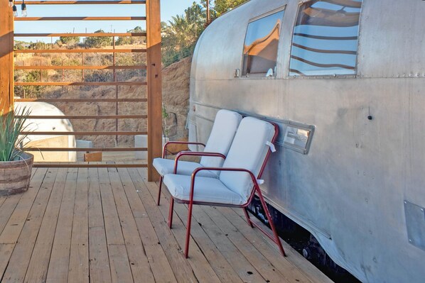 A stationary trailer with a wooden deck, two white cushioned chairs, and a potted plant. - Valley Nomads (Valle de Guadalupe)