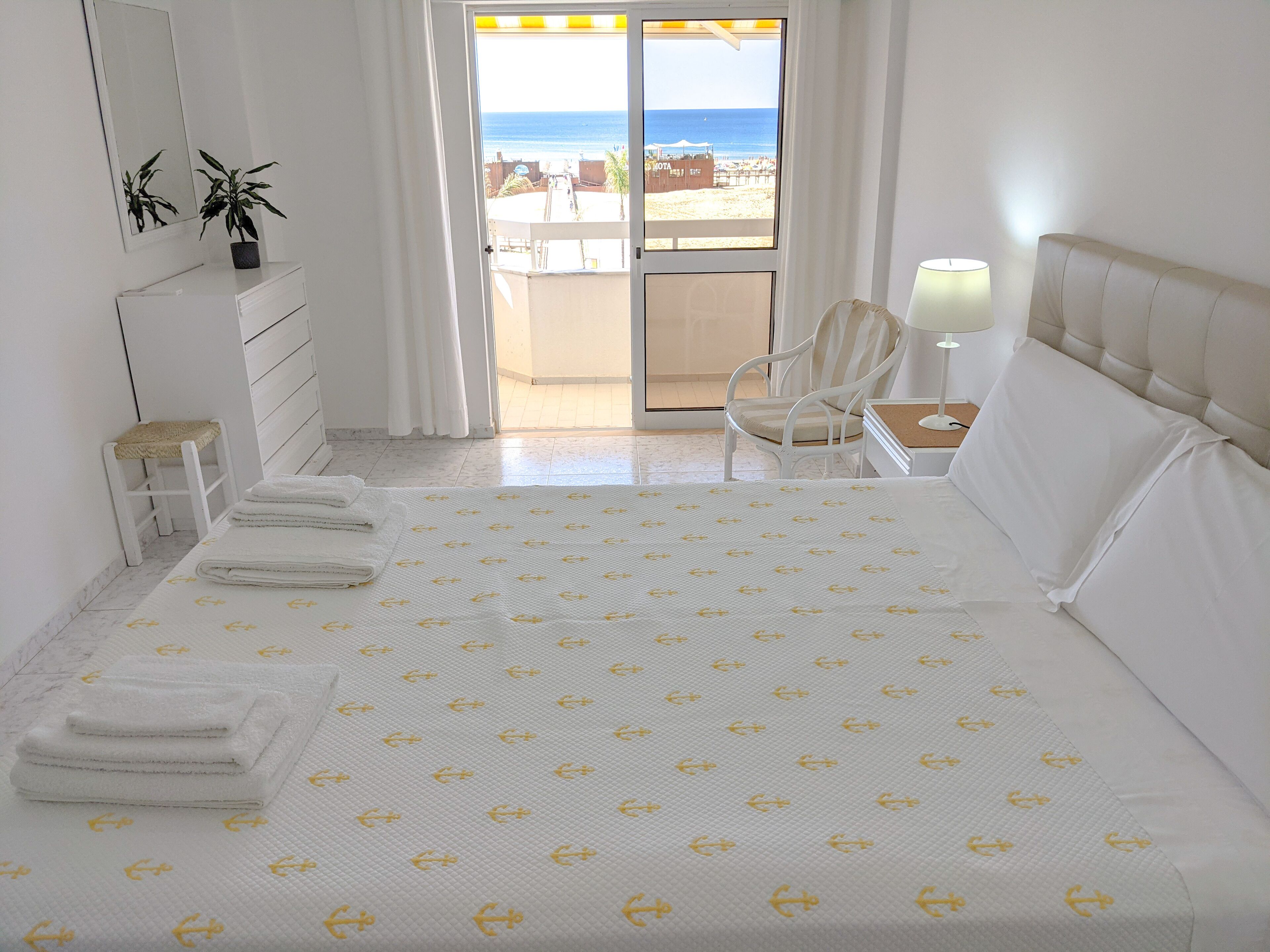 Ein Hotelzimmer mit Bett, Stuhl, Schreibtisch, Lampe, Spiegel und Blick auf den Strand.