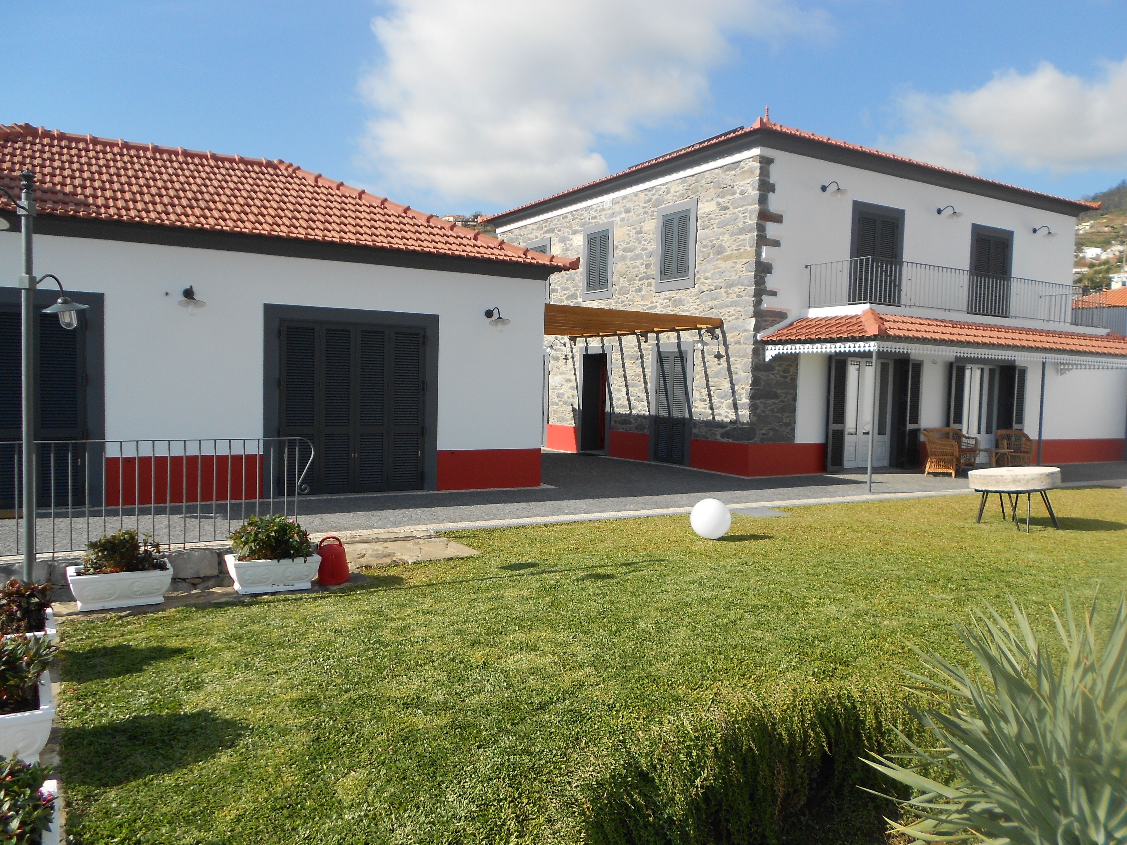 A courtyard with a lawn, a white spherical object, and a building with a red-tiled roof and stone walls.