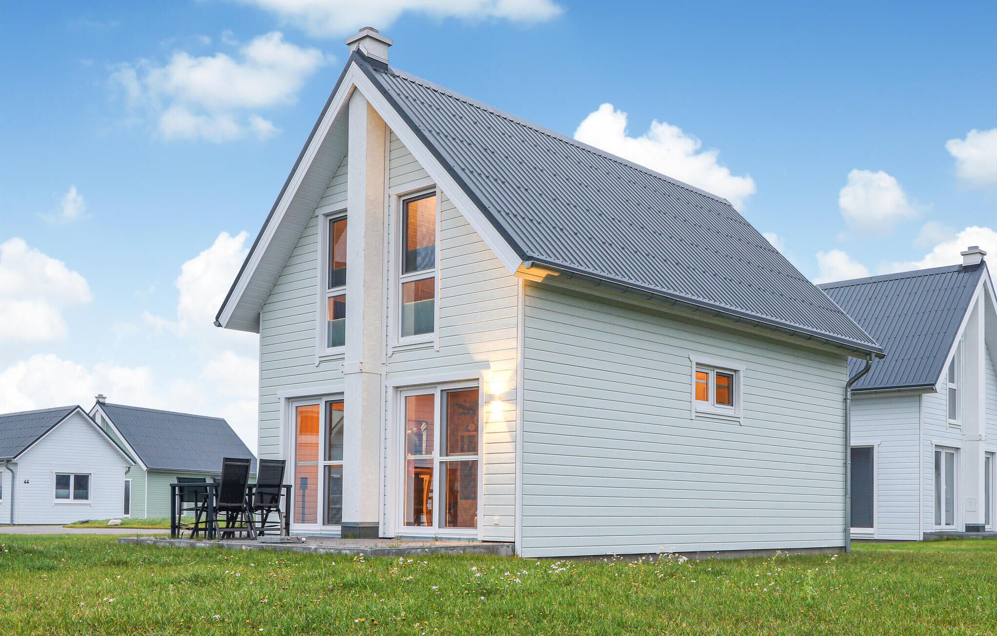 Une maison moderne à deux étages, dotée d’un toit en pente, de grandes fenêtres et d’un espace extérieur aménagé pour se détendre.