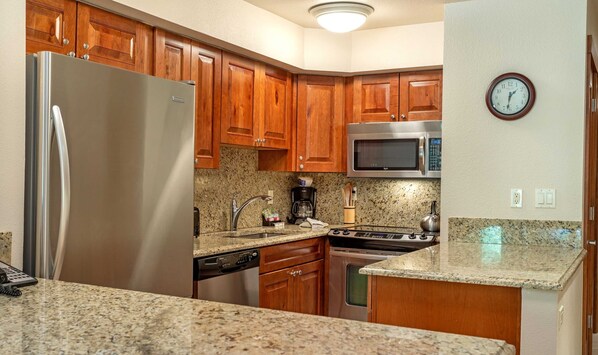 Una cocina con armarios de madera, un refrigerador de acero inoxidable, un microondas, una estufa y encimeras de granito.