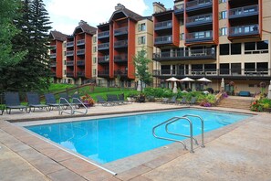 A swimming pool with lounge chairs and umbrellas, surrounded by multi-story buildings with balconies.