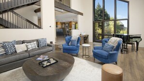 Uma sala de estar ampla com design moderno, apresentando um sofá grande, duas poltronas, uma mesa de centro e um piano.
