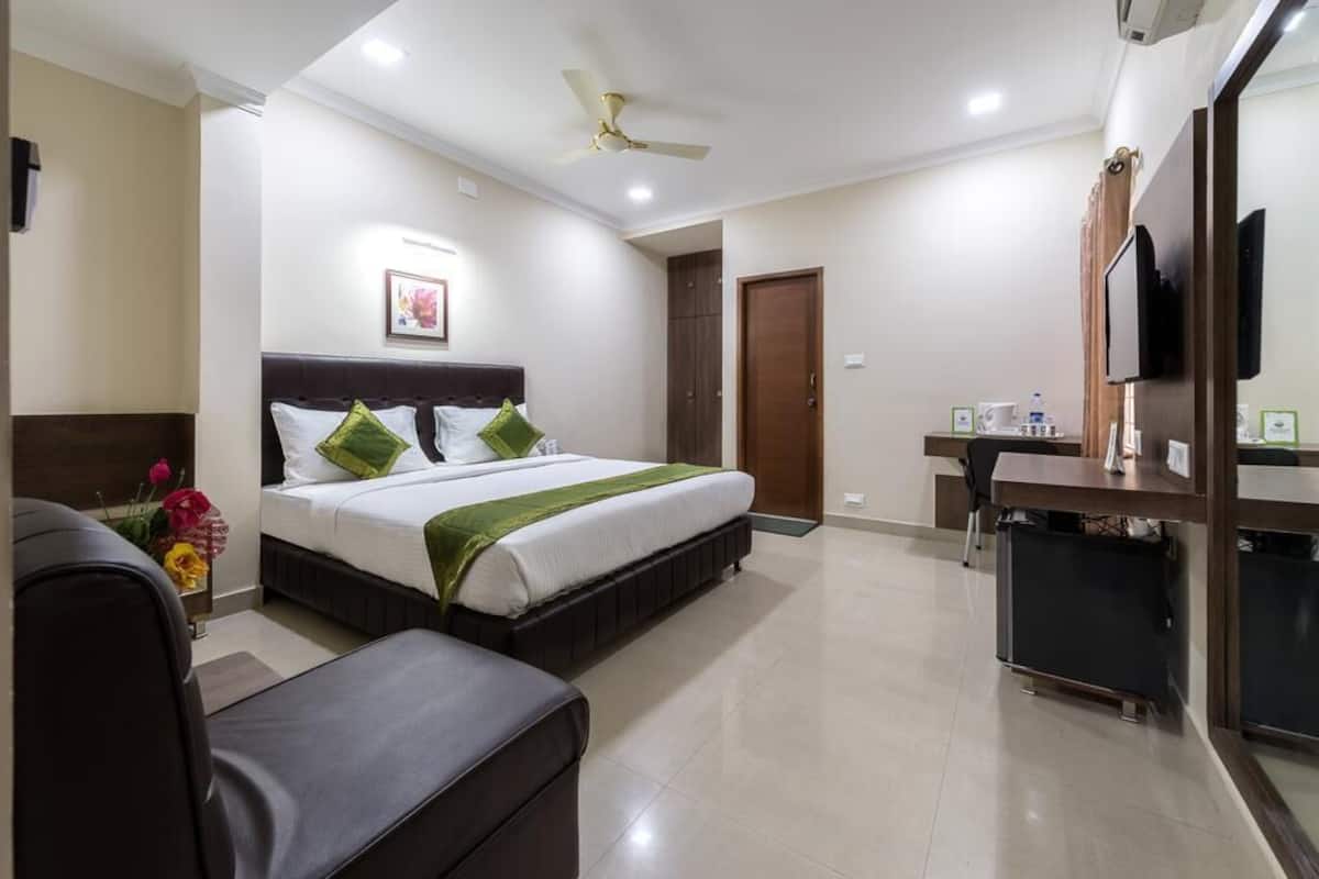 A hotel room with a bed, a desk, a chair, a ceiling fan, and a television.