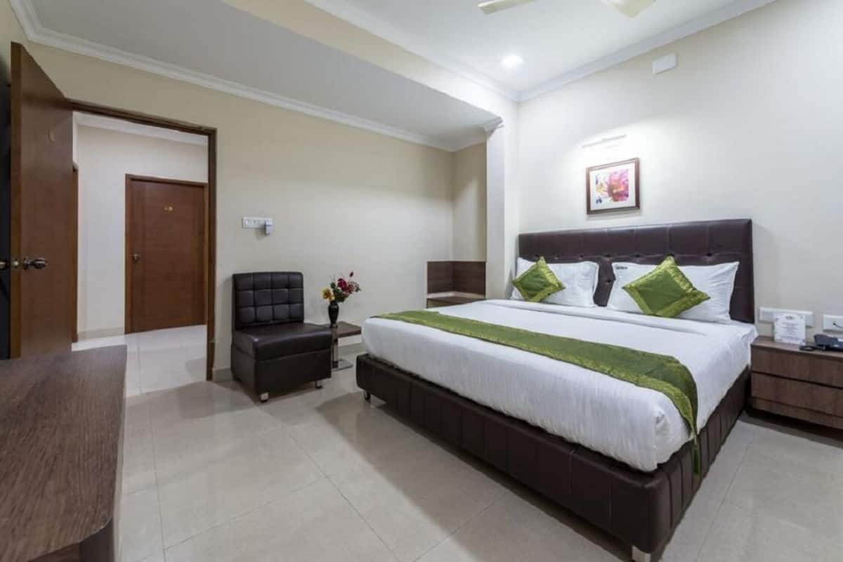 A hotel room with a large bed, a small desk, a chair, and a door.