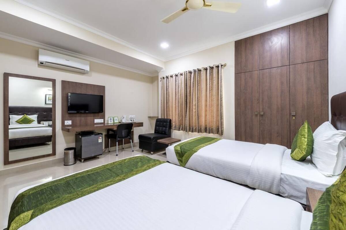 A hotel room with two beds, a desk with a chair, a television, and a wardrobe.