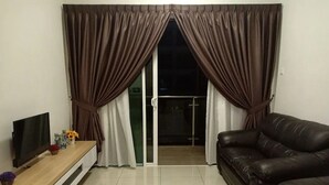 Una sala de estar con televisor, sofá y puerta corrediza de vidrio que da a un balcón.