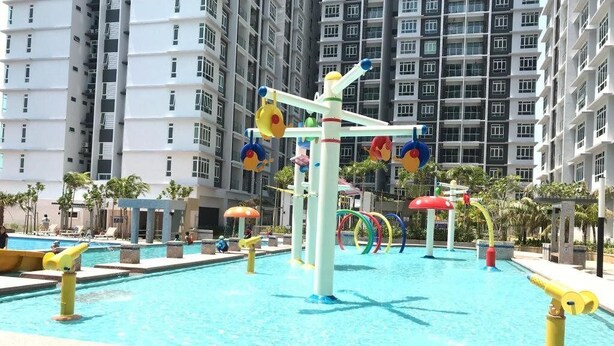 Una piscina con coloridas fuentes y un moderno edificio de apartamentos al fondo.