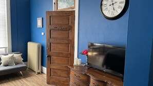 A room with a wooden door, a clock on the wall, a television, and a radiator. - The Clinton Inn (Clinton)