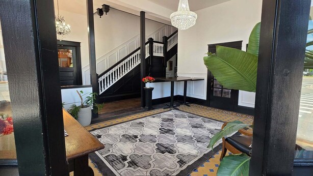 A staircase with a black railing and a chandelier, a patterned rug, and a potted plant. - The Clinton Inn (Clinton)