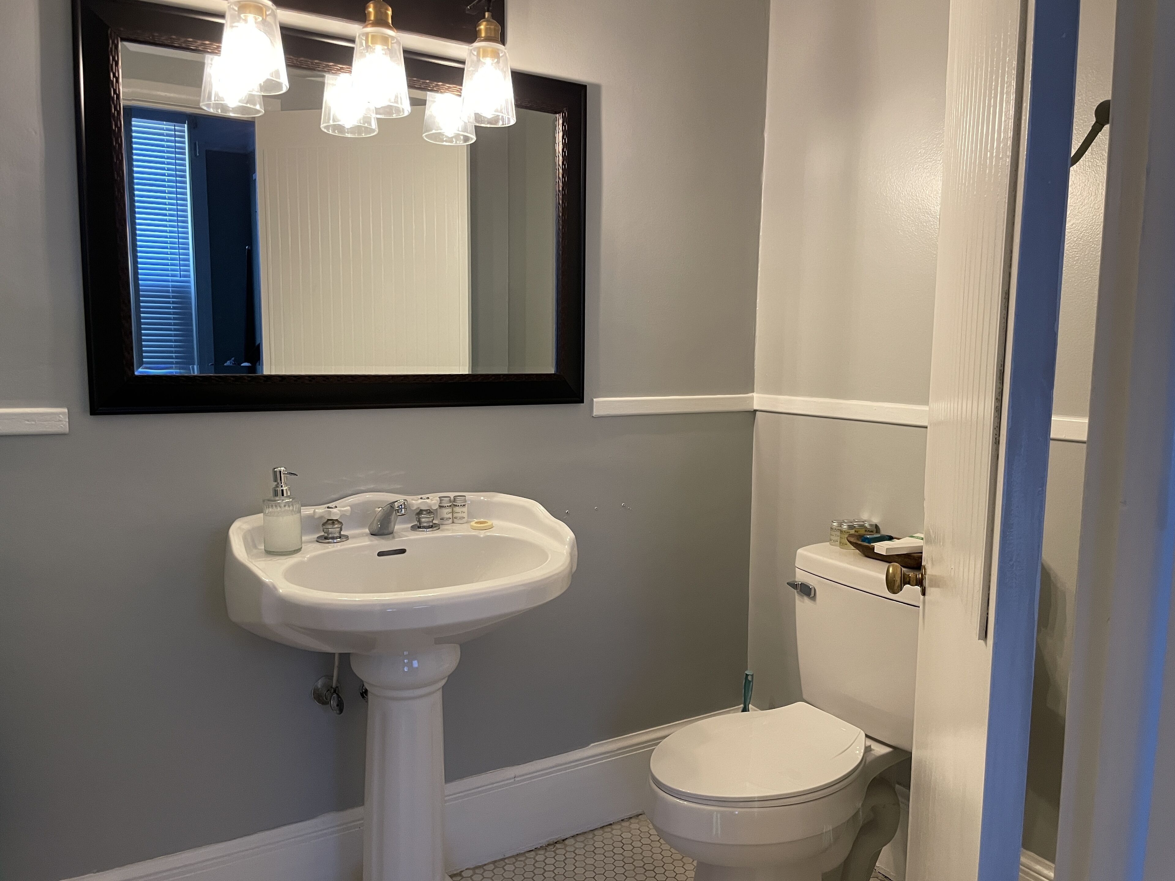 A bathroom with a pedestal sink, a toilet, and a mirror above the sink.