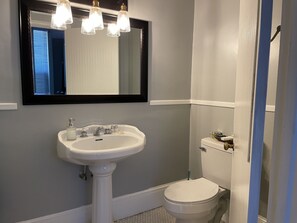 A bathroom with a pedestal sink, a toilet, and a mirror above the sink.