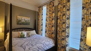 Uma cama com dossel com colcha florida, um criado-mudo com abajur e um quadro na parede.