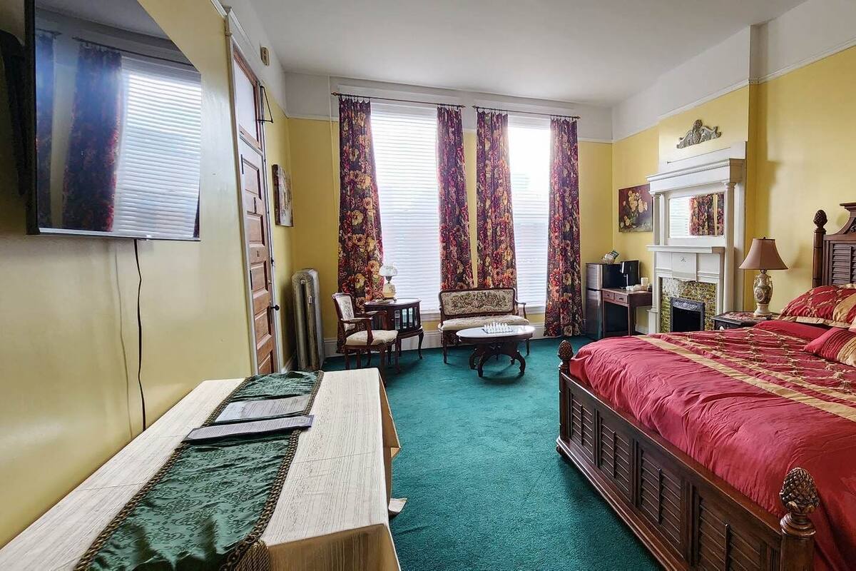 A bedroom with a large bed, a wooden headboard, a television mounted on the wall, and a fireplace.