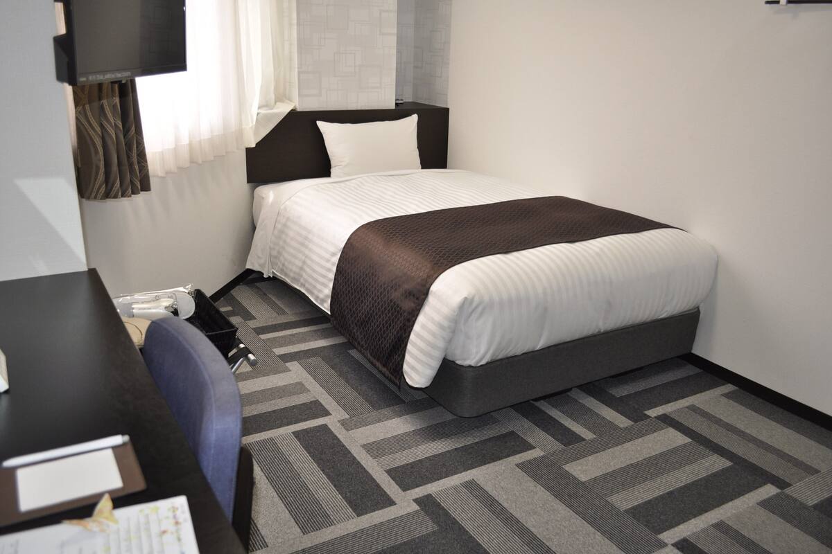 A hotel room with a bed, a desk, and a chair.