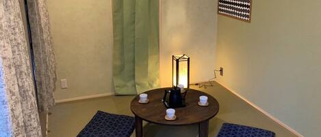 A room with tatami flooring, a low table with cups and a tea set, and a traditional Japanese lantern.