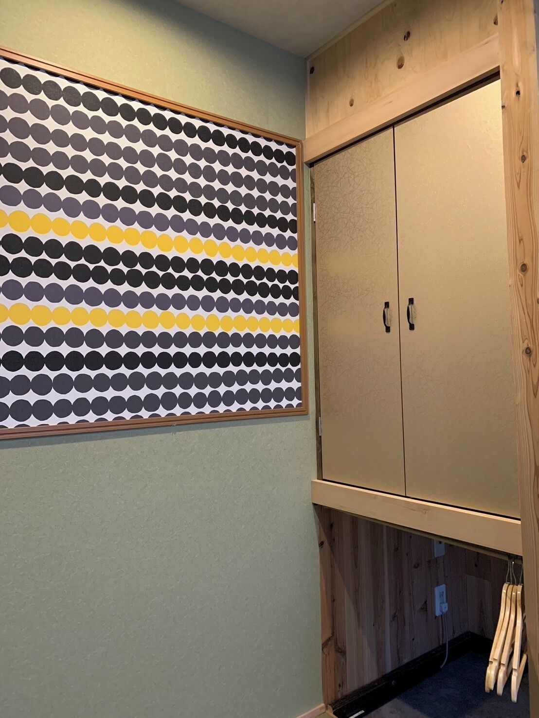 A room with a wooden wardrobe, a patterned wall, and a wooden floor.
