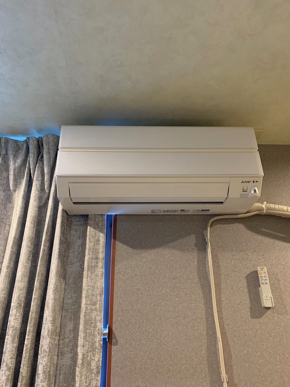 A white air conditioning unit mounted on a wall, connected to a power outlet and a control panel.