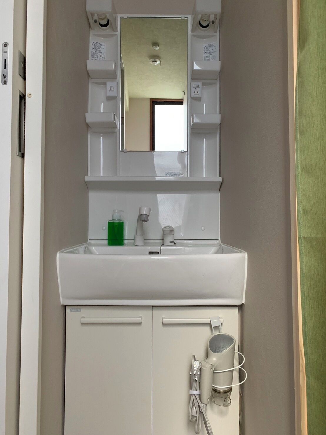 A bathroom with a white sink, mirror, and cabinet. There is a green bottle and a white cup on the sink.