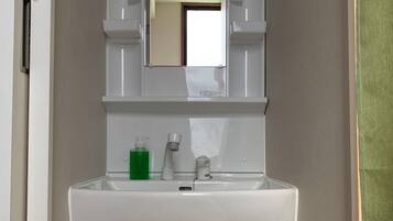 A bathroom with a white sink, mirror, and cabinet. There is a green bottle and a white cup on the sink.