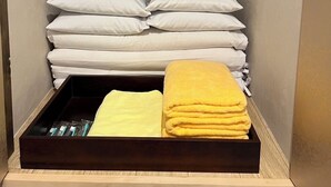 A small, compact bedroom with a bed, pillows, and a wooden bench with towels. - HOTEL PRELE SHINKAN (Tokyo)