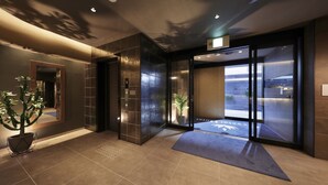 A modern hotel lobby with a reception desk, a potted plant, and a glass door entrance. - Doutonbori Crystal Hotel IV (Osaka)