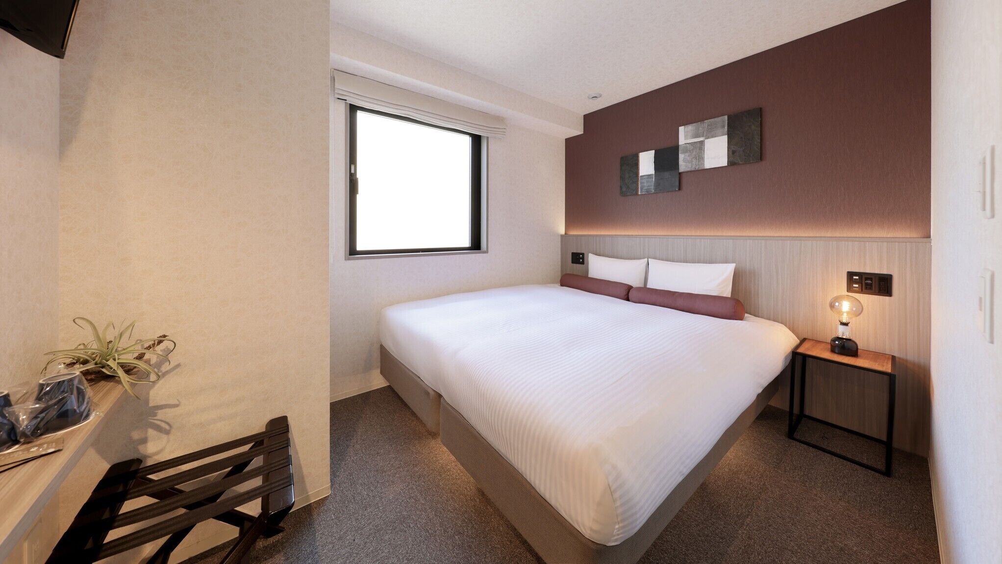 Una habitación de hotel con cama, mesita de noche, lámpara y ventana.