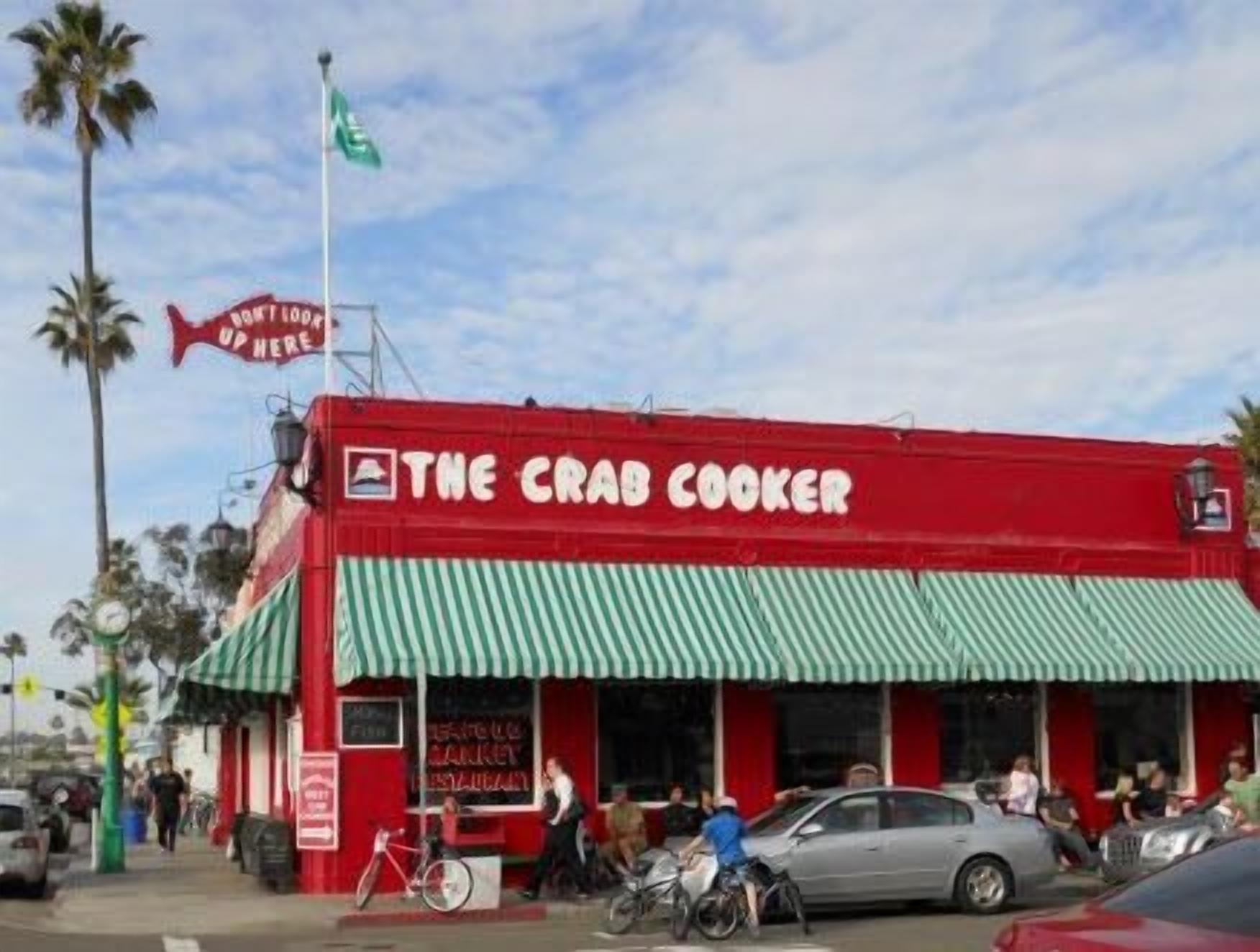 A red building with a green and white striped awning labeled "The Crad Cooker".