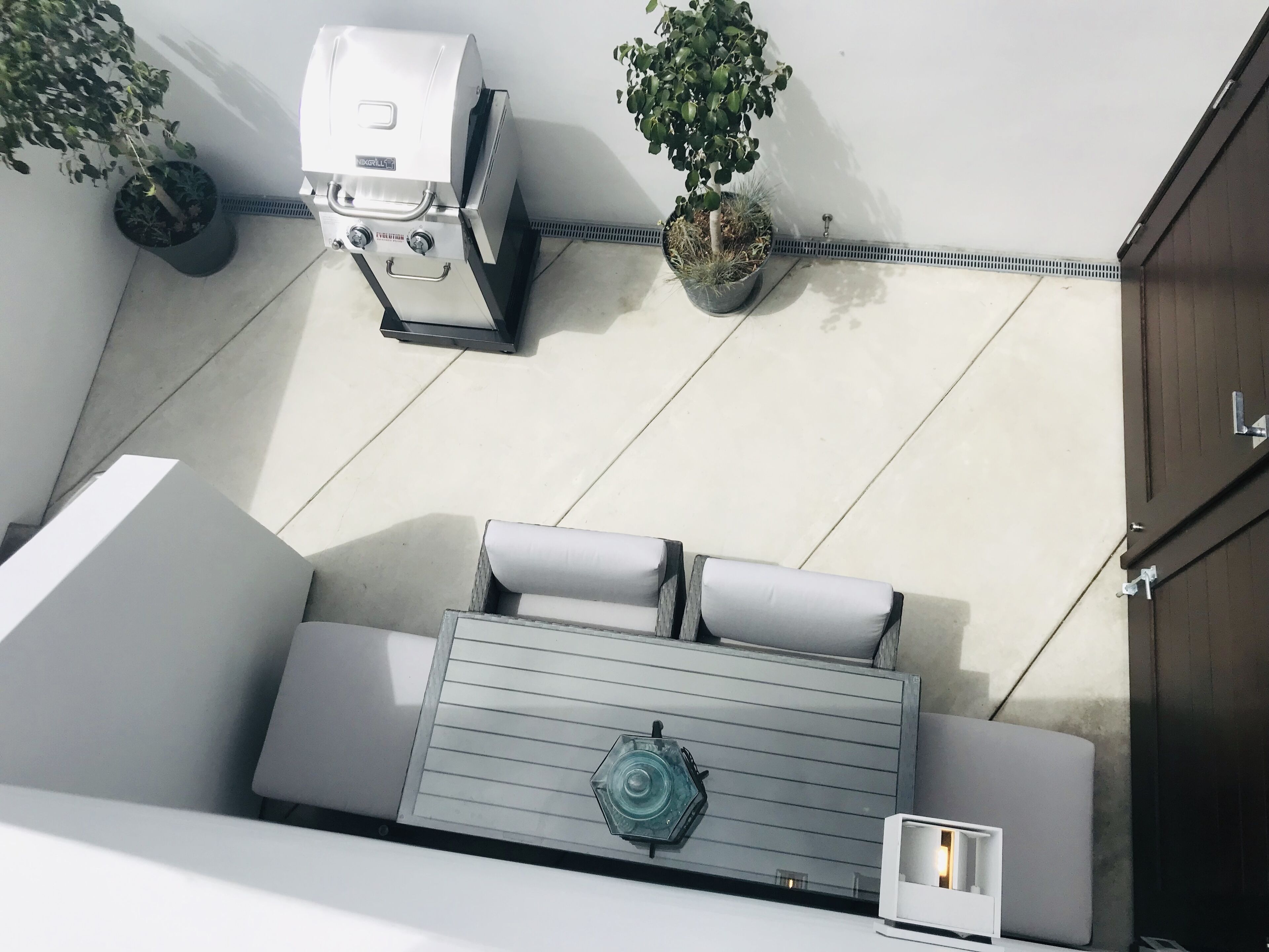 Une terrasse sur le toit équipée d’un barbecue, de deux plantes en pot, d’un coin salon avec des coussins et d’une petite table.