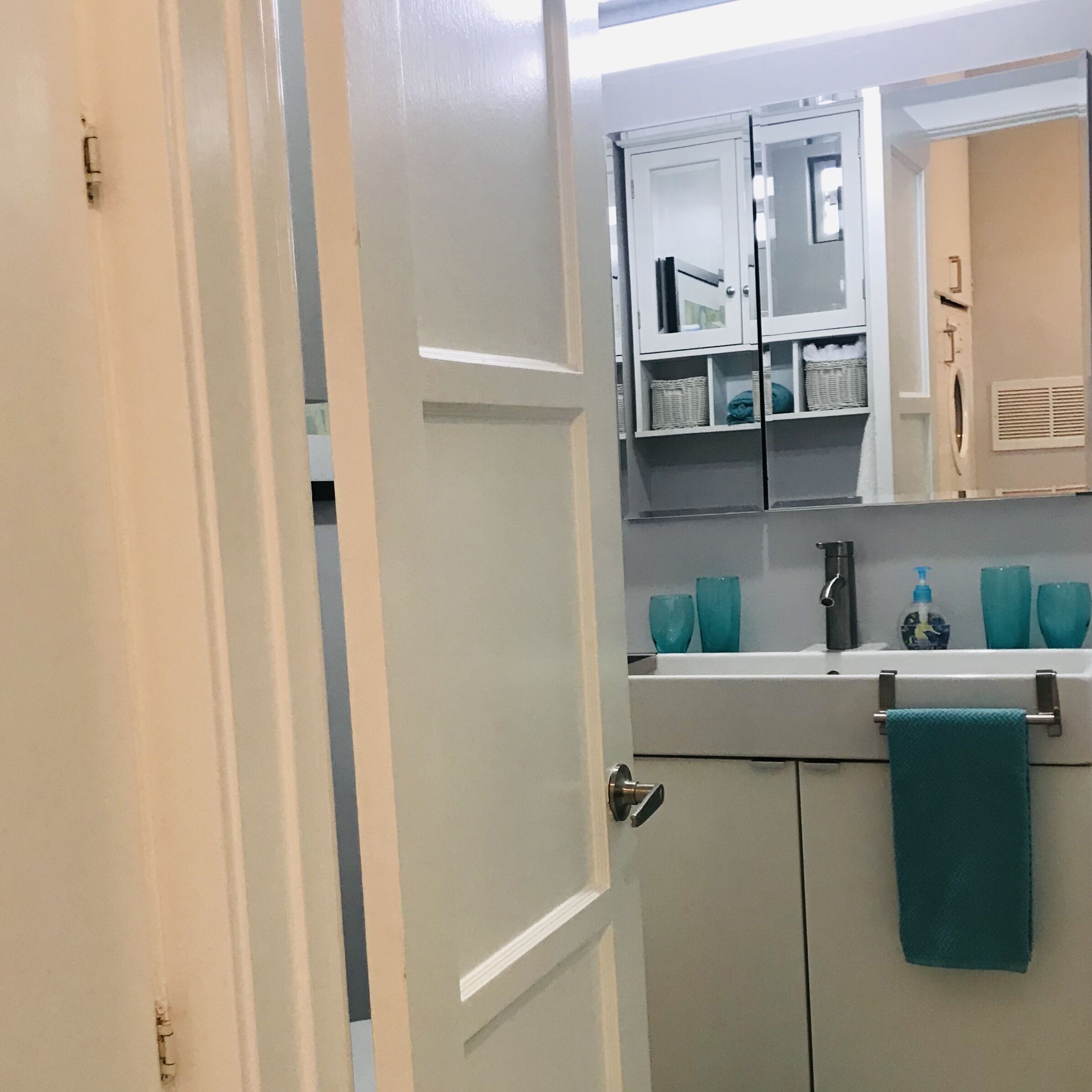 Un baño con una puerta blanca, un lavamanos con toallero y un espejo sobre el mueble del lavabo.