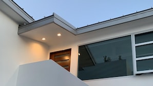 Um edifício moderno com telhado inclinado, uma janela grande e um acessório de iluminação na parede externa.
