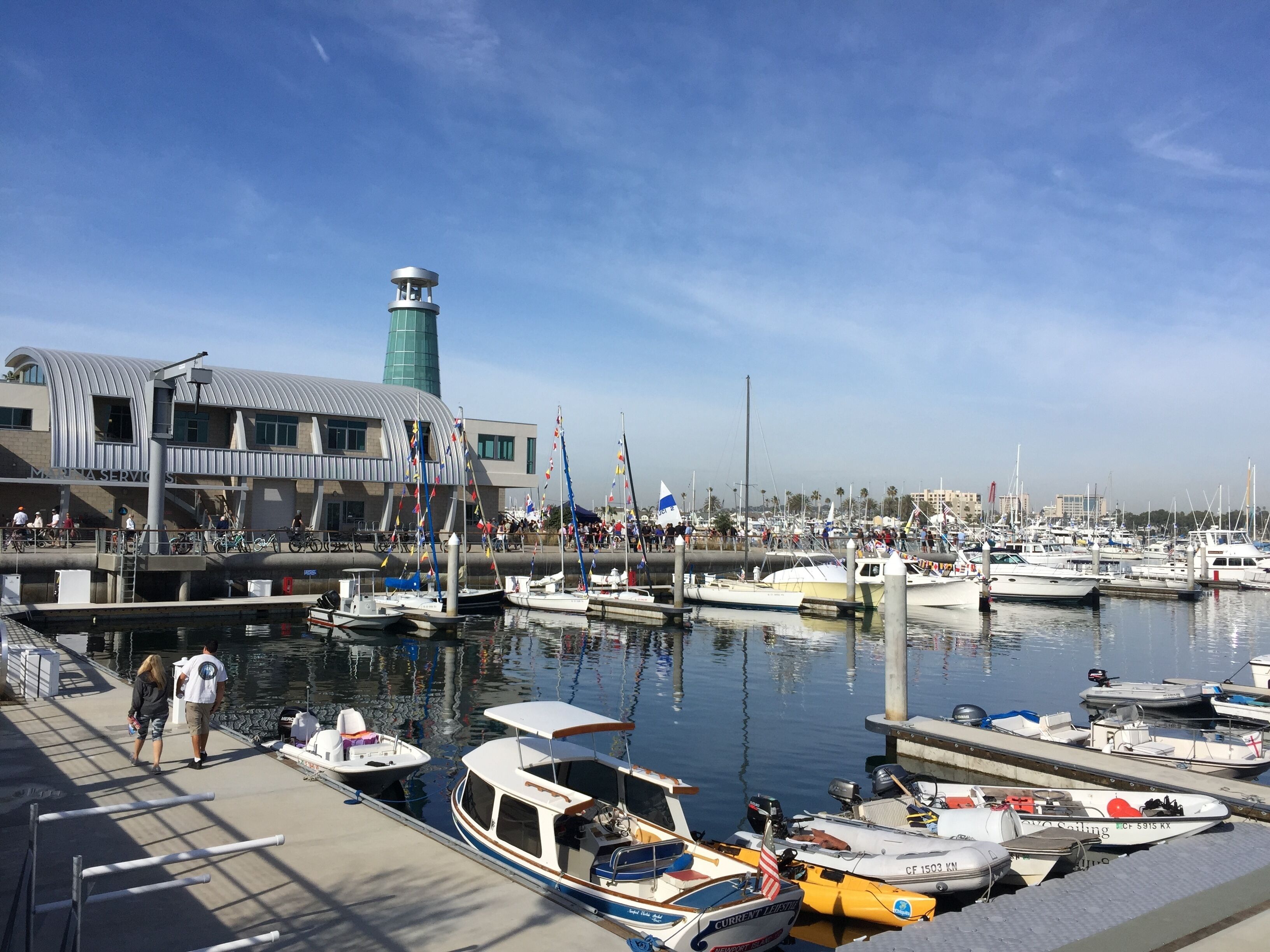 Un puerto deportivo con barcos amarrados, un edificio con una torre verde y un paseo peatonal.