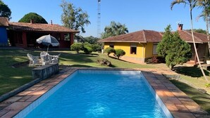 Une piscine entourée de carreaux de pierre, avec une pelouse et un bâtiment jaune en arrière-plan.