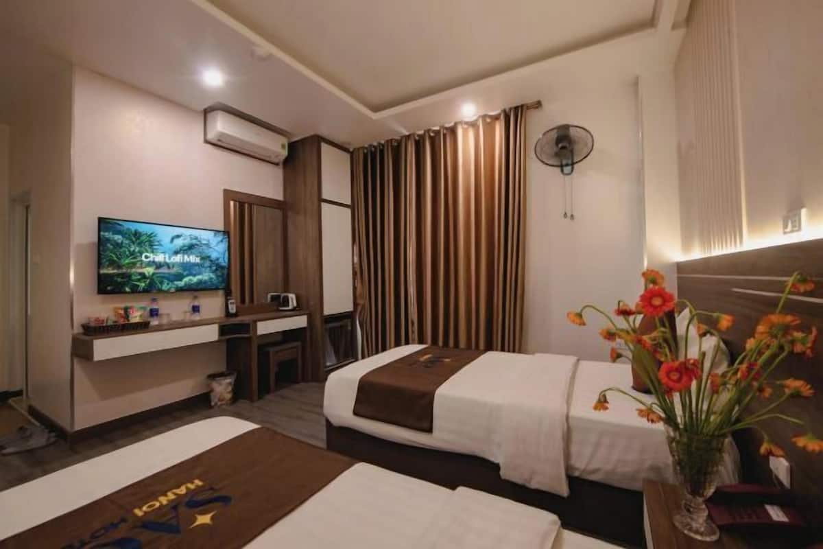 A hotel room with two beds, a TV, a desk, a mirror, and a window with curtains.