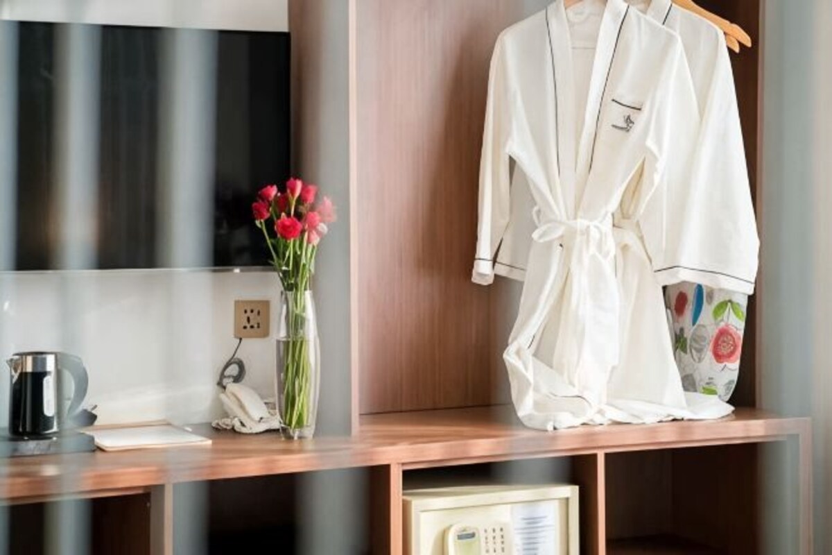 Un bureau en bois, sur lequel se trouvent un vase de fleurs, un téléphone et une robe blanche suspendue à un porte-manteau.