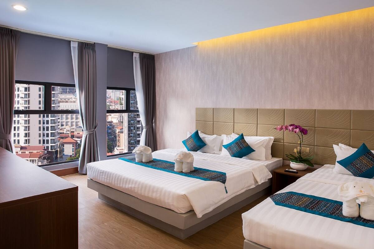 Ein Hotelzimmer mit zwei Betten, einem Schreibtisch und Blick auf die Stadt.