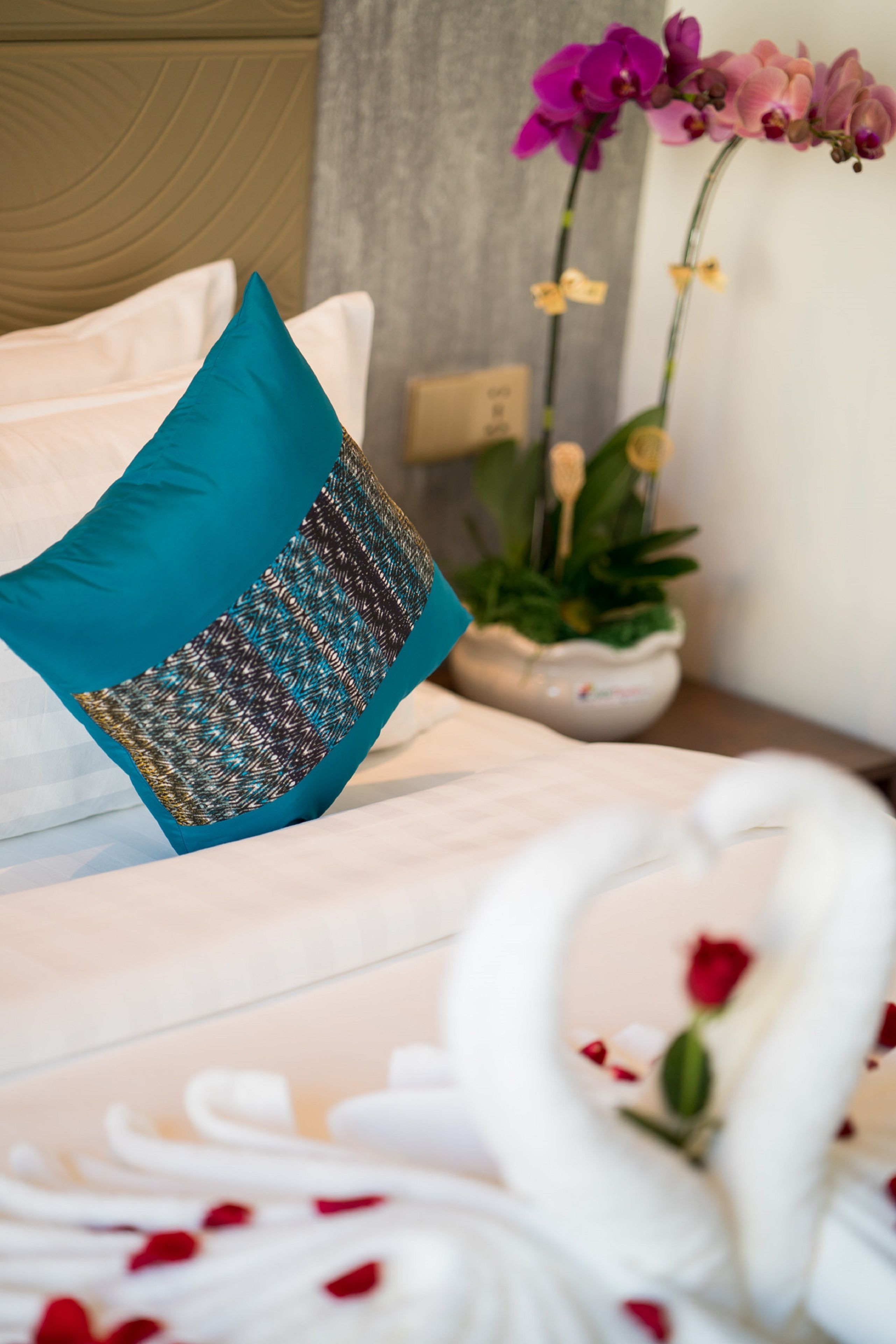 A bed with a teal pillow, a white swan decoration, and a potted orchid plant.