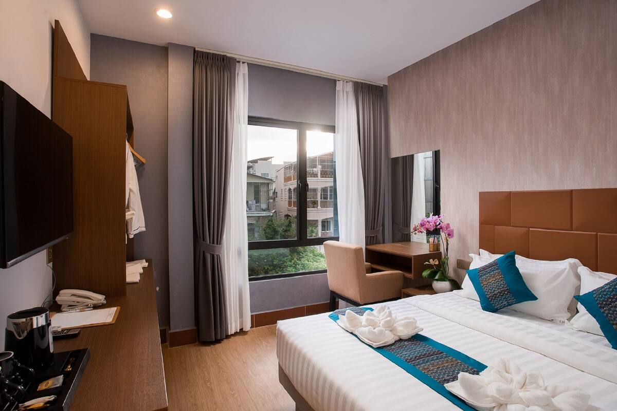Ein Hotelzimmer mit Bett, Schreibtisch, Stuhl, Fernseher und einem Fenster mit Vorhängen.