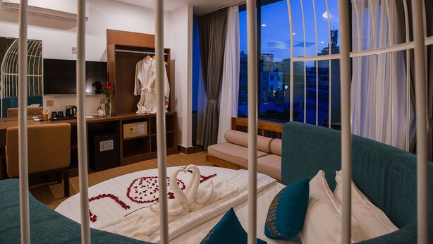 A hotel room with a bed, a desk, a wardrobe, and a large window with a city view. - Orussey One Boutique (Phnom Penh)