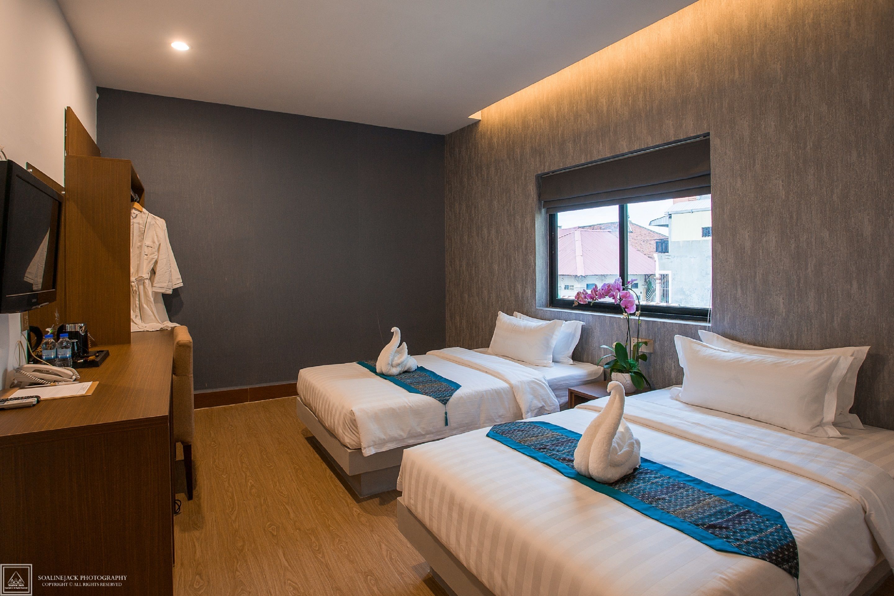 A hotel room with two beds, a desk, a mirror, and a window with a view of buildings.