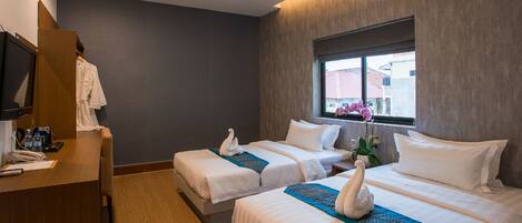 A hotel room with two beds, a desk, a mirror, and a window with a view of buildings.