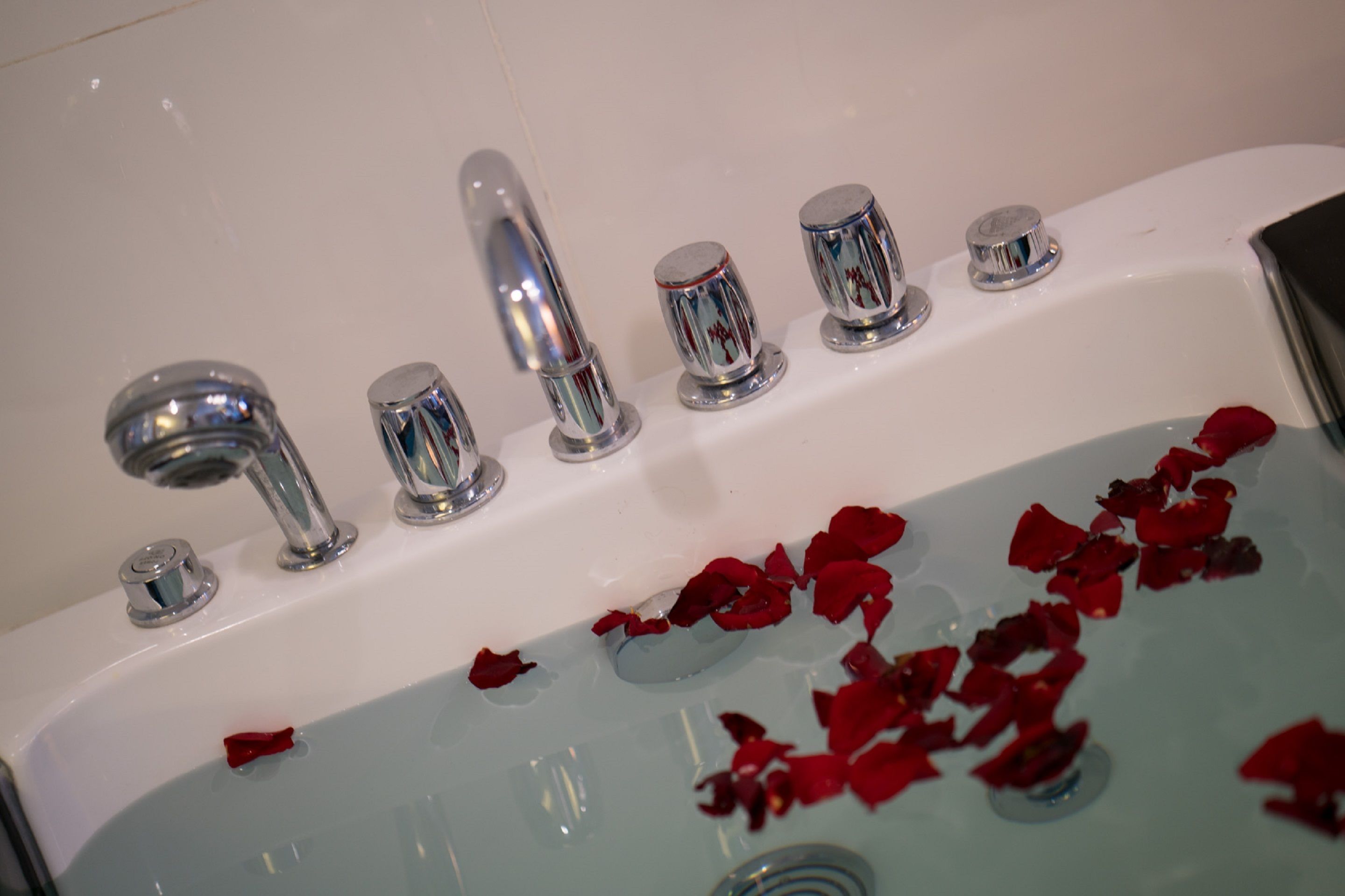 A bathtub with rose petals floating in the water and chrome fixtures.