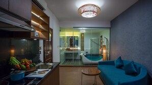 A modern kitchen with a dining area, a glass-enclosed bathroom with a bathtub, and a blue sofa. - Orussey One Boutique (Phnom Penh)
