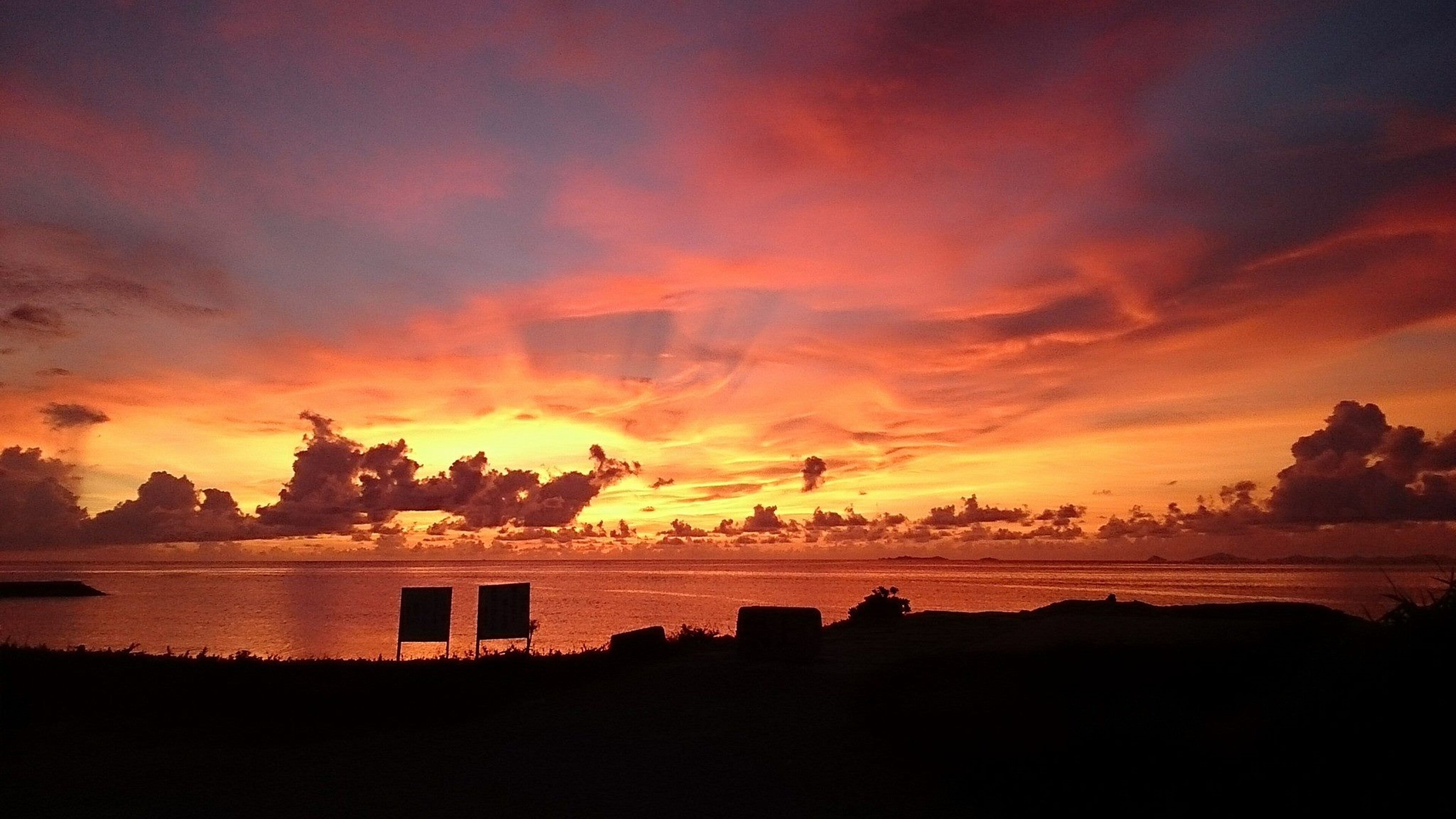 Een zonsondergang boven een wateroppervlak met twee lege stoelen op de voorgrond.