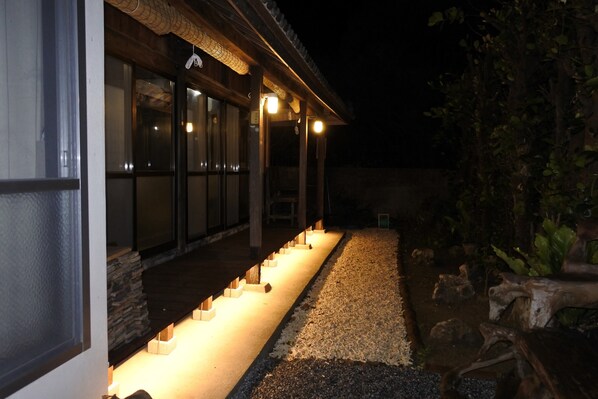 A building with a covered outdoor area, stone steps leading to a door, and a gravel path.