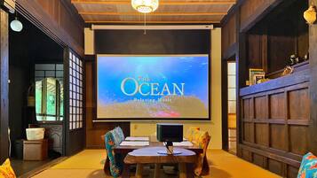A room with a large screen displaying 'The Ocean' music, a wooden table, colorful chairs, and traditional decor.