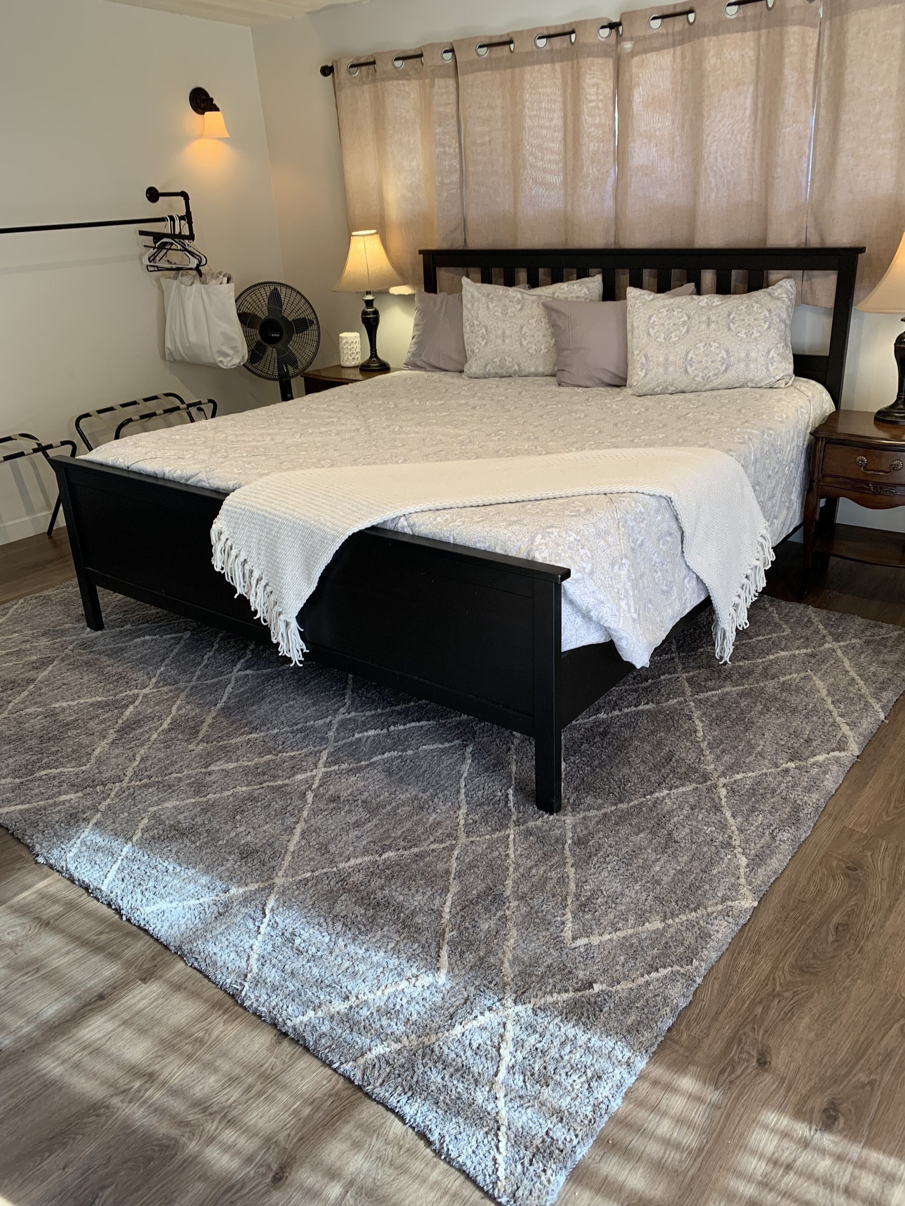 A bedroom with a bed, a nightstand, a lamp, a fan, and a wall-mounted light fixture.